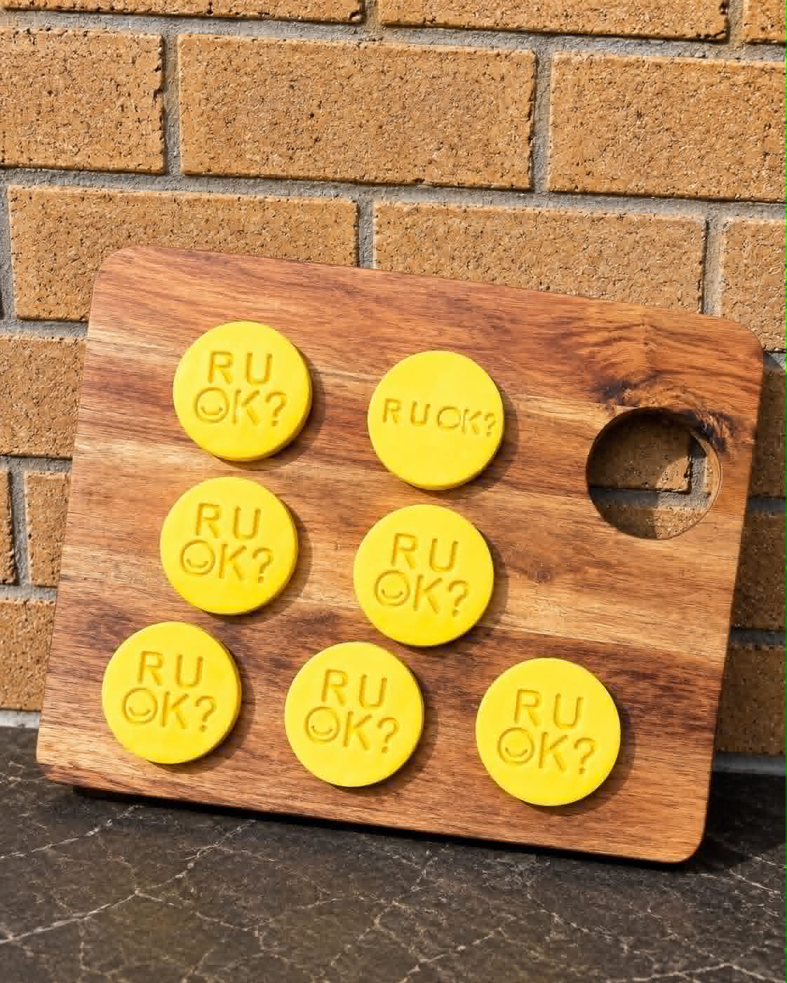Yellow round R U OK? Day stamped sugar cookies with smiley face on a wooden board against a brick wall
